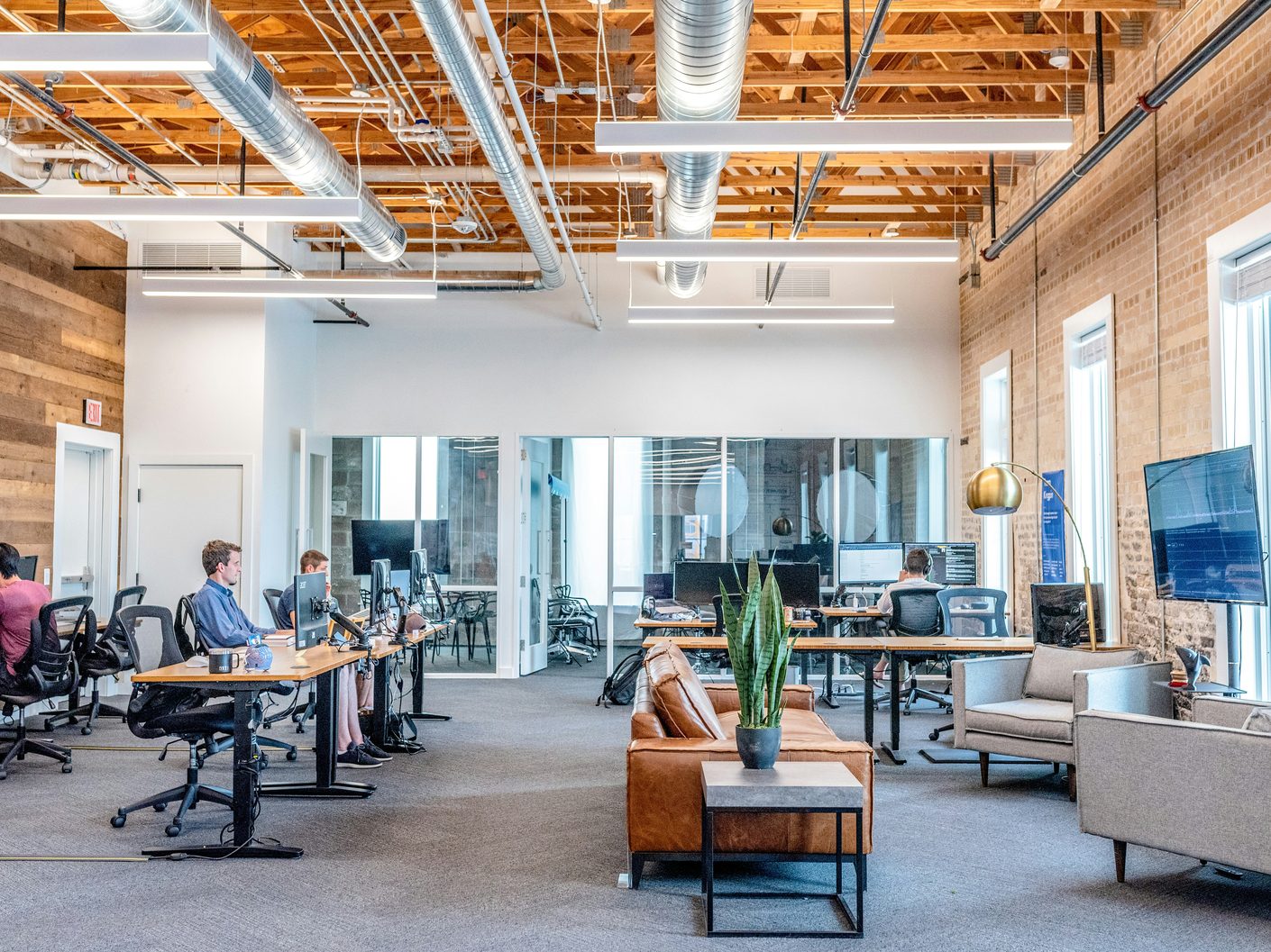 A bright open-plan office with exposed timber ceiling joists, long shared desks and a tan leather sofa