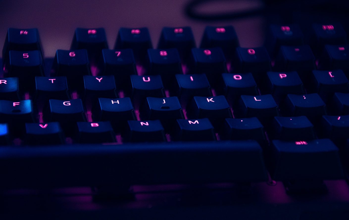 Close-up of a backlit mechanical keyboard glowing pink and blue in darkness with shallow focus