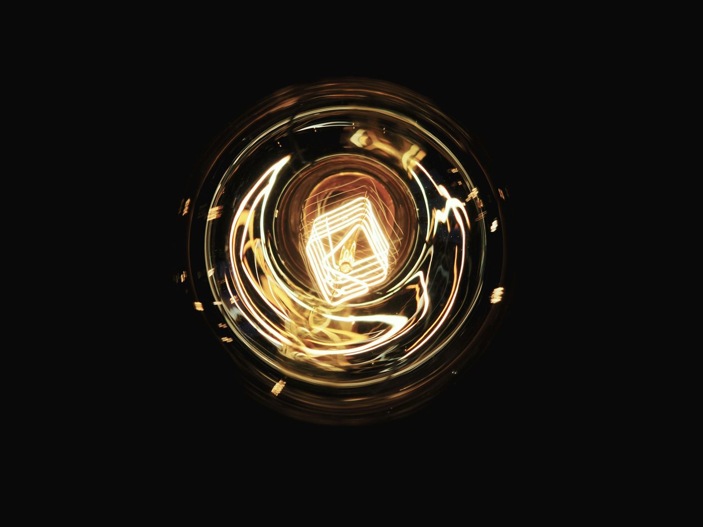 A glowing filament inside a clear light bulb against a solid black background in warm amber tones